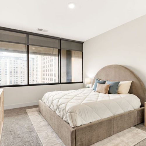 Bedroom with large windows and a dresser with decor in front of the bed
